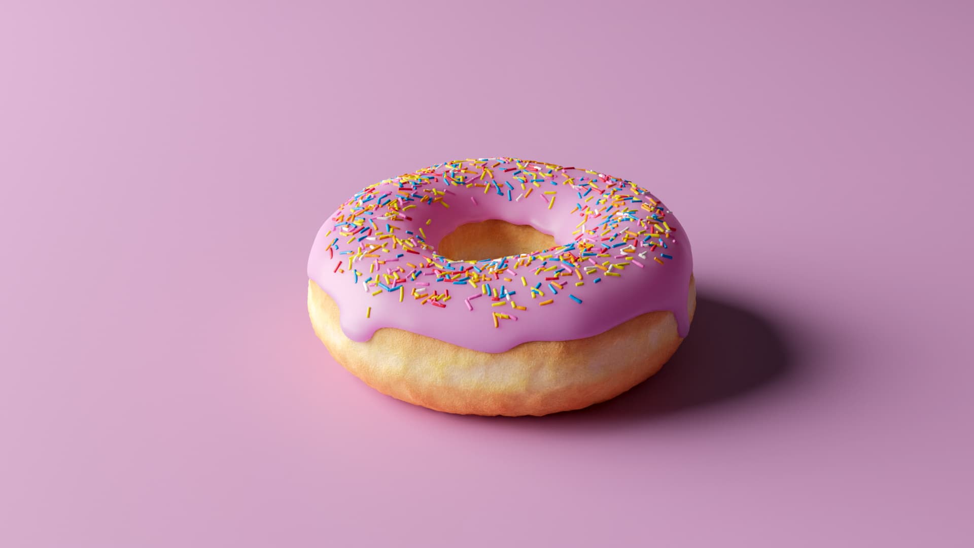 An image of a donut in a pink background with a pink icing on top with several colorful sprinkles.